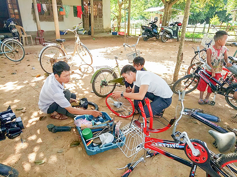 Anh Dũng (phía trái ảnh) và một thầy giáo Trường THCS Tân Lập, huyện Hướng Hóa sửa xe miễn phí cho các em học sinh ở bản Cồn​